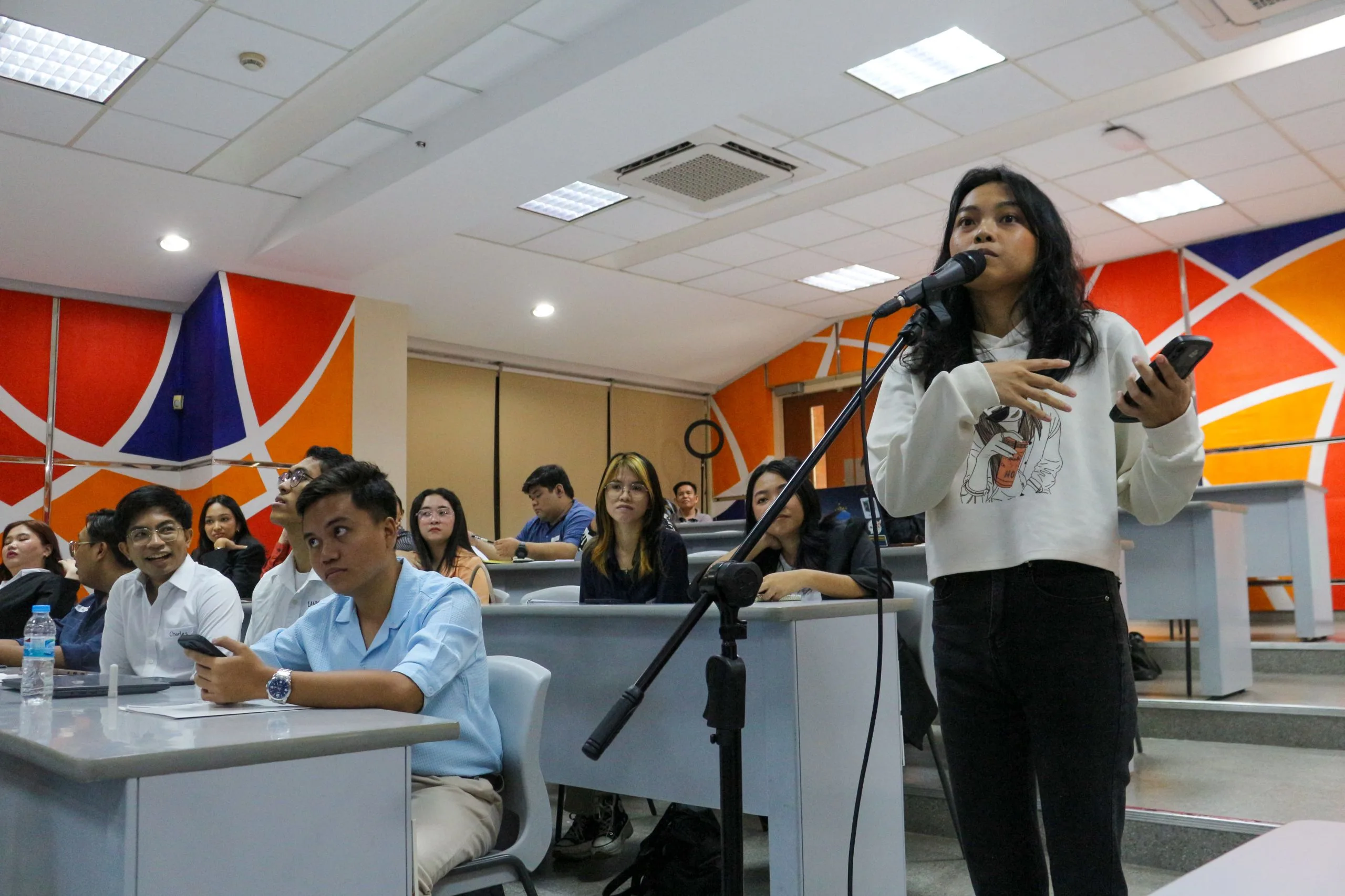 A student standing at a microphone to ask a question during an Aiducation Pathway to Higher Education event in the Philippines, with fellow participants seated behind her